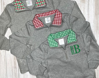 May include: Three gray quarter-zip sweatshirts with different colored gingham collars. The collars are red and green, red and white, and green and white. The bottom sweatshirt has the monogram "BHB" embroidered on the front in green.