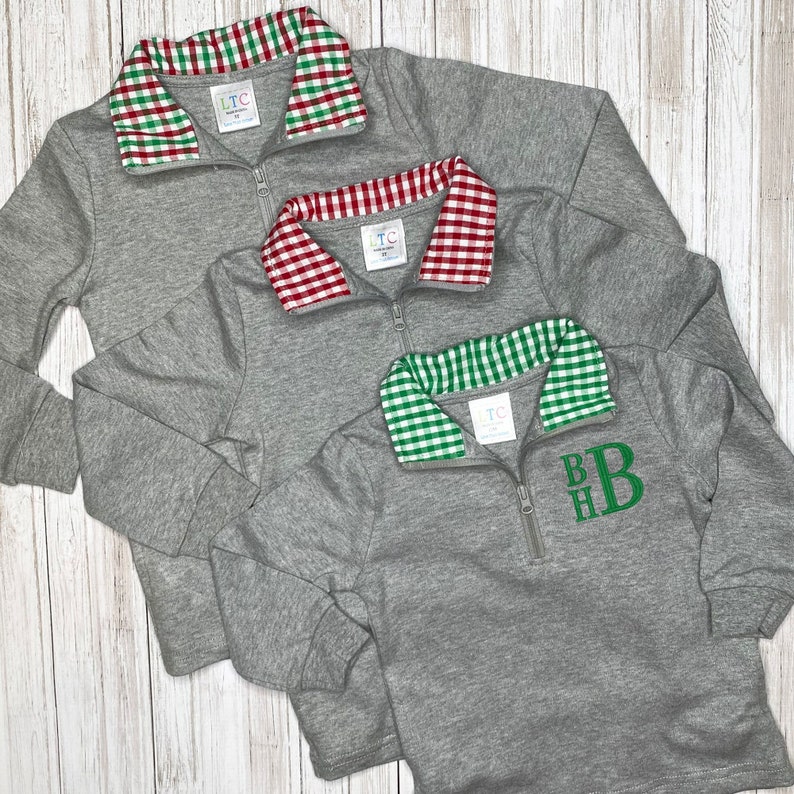 May include: Three gray quarter-zip sweatshirts with different colored gingham collars. The collars are red and green, red and white, and green and white. The bottom sweatshirt has the monogram "BHB" embroidered on the front in green.