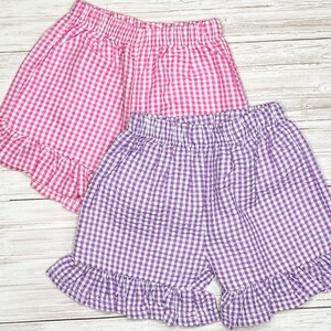 May include: Two pairs of gingham shorts with ruffled hems. One pair is pink and white gingham, the other is purple and white gingham.