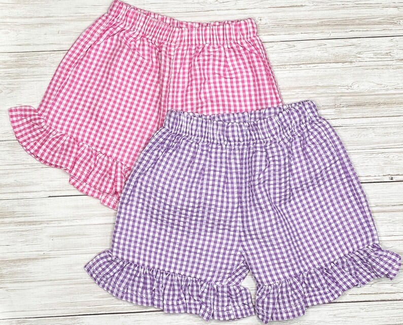 May include: Two pairs of gingham shorts with ruffled hems. One pair is pink and white gingham, the other is purple and white gingham.