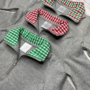 May include: Three gray quarter-zip sweatshirts with different colored gingham collars. The collars are red and white, green and white, and green and white. The sweatshirts have a zipper closure and the text "LTC" on the collar.