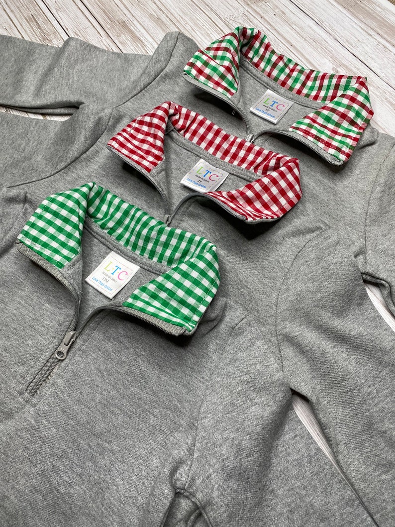 May include: Three gray quarter-zip sweatshirts with different colored gingham collars. The collars are red and white, green and white, and green and white. The sweatshirts have a zipper closure and the text "LTC" on the collar.