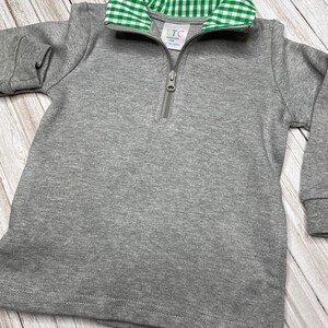 May include: Gray long-sleeve pullover with a green and white gingham collar. The pullover has a zipper closure and a small tag that says "LTC Made in China 12M"
