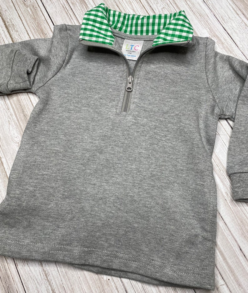 May include: Gray long-sleeve pullover with a green and white gingham collar. The pullover has a zipper closure and a small tag that says "LTC Made in China 12M"