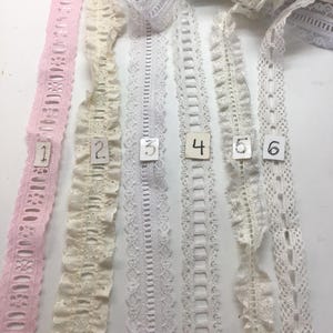 May include: Assortment of lace ribbons in various designs and colors, including pink, cream, and white. Each ribbon is numbered from 1 to 6. The ribbons are displayed on a white surface, showcasing their intricate patterns and textures. Ideal for crafting and sewing projects.