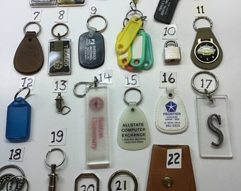 May include: A collection of 22 keychains with various designs, including a rainbow, a cartoon character, a lock, a car logo, and a letter S. The keychains are numbered 1 through 22.