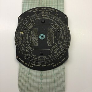 May include: A black circular dead reckoning computer with a white dial and markings. The dial has scales for air speed, air temperature, pressure altitude, and altitude computations. The computer is labeled "Dead Reckoning Computer" and "Specification AN-C-74".