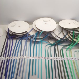 May include: A collection of 30 spools of ribbon in various shades of blue, green, and teal. The spools are numbered 1 through 30.