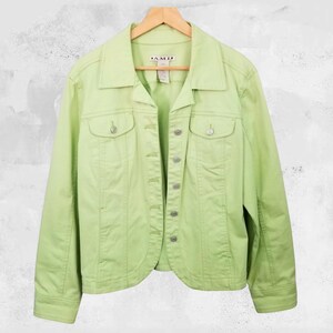 May include: A light green jacket with a button-up front, two chest pockets, and a collared neckline. The jacket is hanging on a wooden hanger against a neutral background. The jacket has the brand name "A.M.I." on the tag.