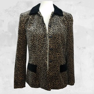 May include: A button-down blazer with a leopard print pattern in shades of brown and black. The blazer features a black velvet collar and two black pockets. The garment is displayed on a mannequin.