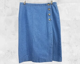 May include: A light blue denim skirt with a wrap-style design. The skirt features a series of four gold-colored buttons on the side for closure. The skirt is hanging on a metal hanger against a neutral background.