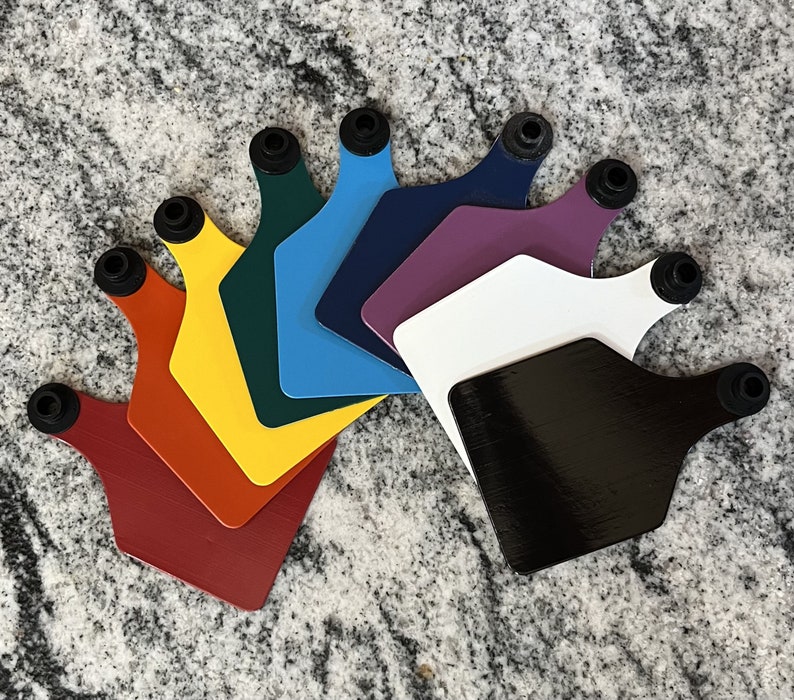May include: A set of nine colourful plastic ear tags with black rubber rings. The tags are arranged in a fan shape, with the darkest tag at the bottom and the lightest tag at the top.