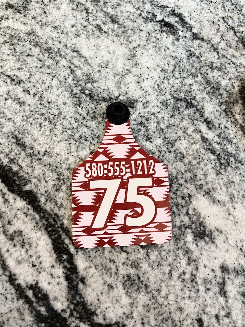 May include: Red and white patterned plastic livestock tag with the number 75 and the phone number 580-555-1212 printed on it.