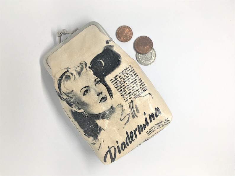 May include: A vintage-style coin purse with a cream-colored fabric exterior. The purse features a black and white illustration of a woman with a glamorous hairstyle and a bold black and white text that reads "Diademina".