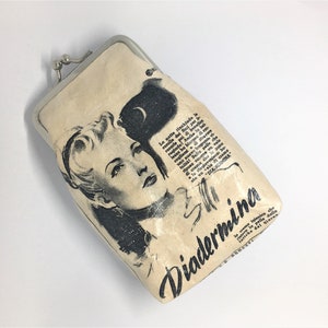 May include: A vintage-style cream-colored coin purse with a silver clasp. The purse features a black and white illustration of a woman with the text "Diadermina" printed on the front.