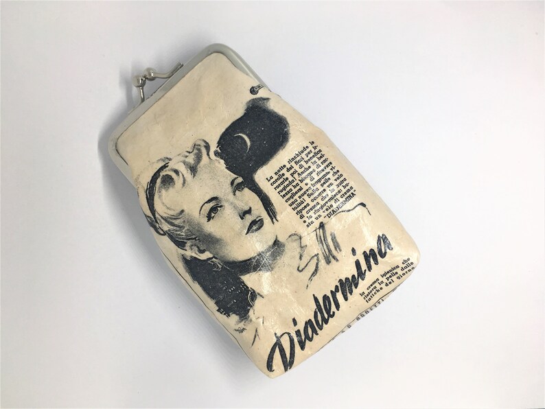 May include: A vintage-style cream-colored coin purse with a silver clasp. The purse features a black and white illustration of a woman with the text "Diadermina" printed on the front.