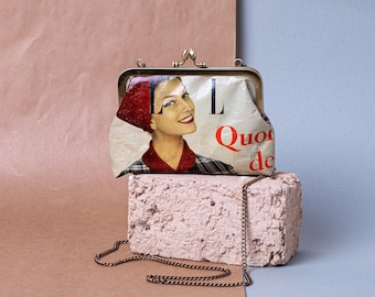 May include: A vintage-style clutch purse with a gold chain strap. The purse is made of a cream-colored material with a red and black magazine cover design featuring a woman and the text "L'L Quoi de".