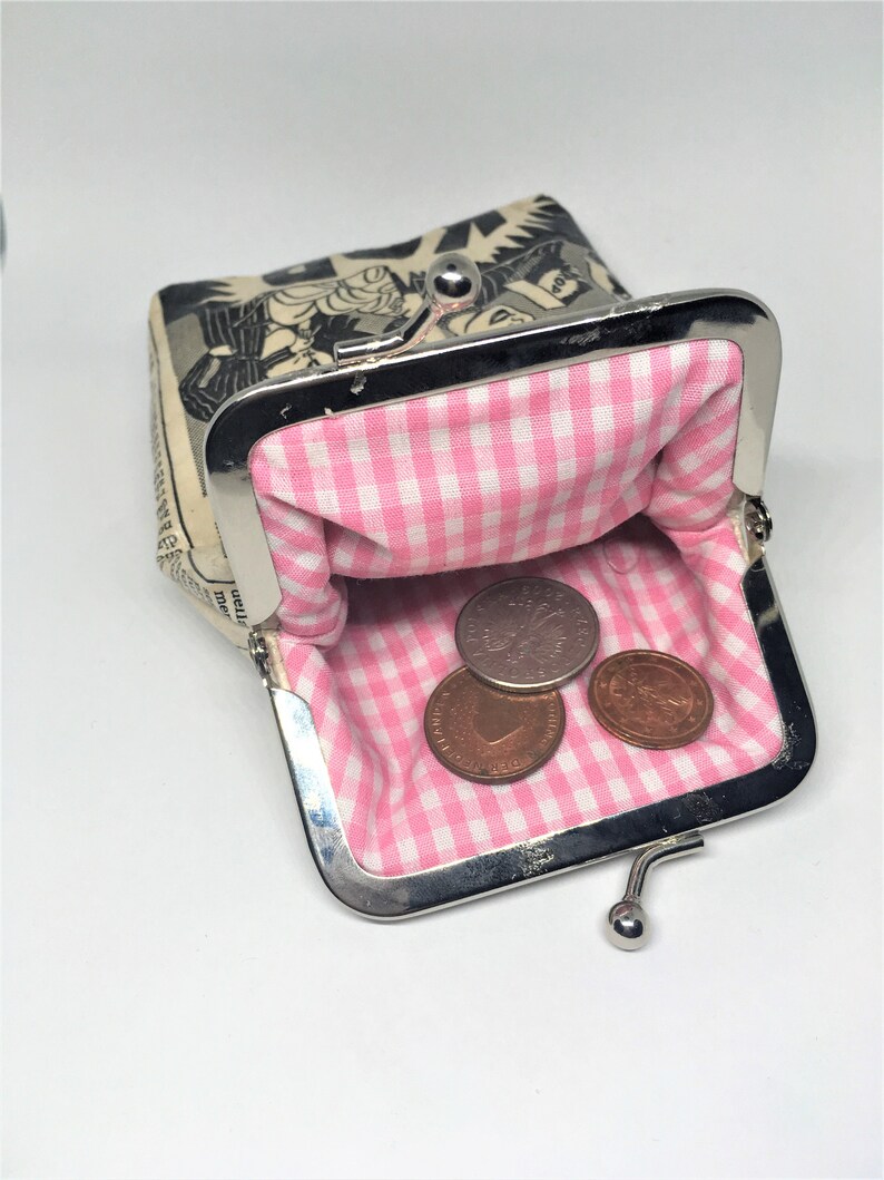 May include: A small, black and white comic book print coin purse with a pink and white gingham lining. The purse is open and has three coins inside.