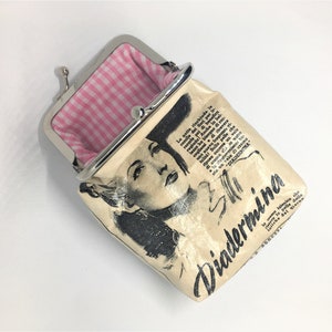 May include: A small, cream-colored coin purse with a silver clasp. The purse has a black and white image of a woman on the front, along with the text "Diadermina". The inside of the purse is lined with pink and white gingham.
