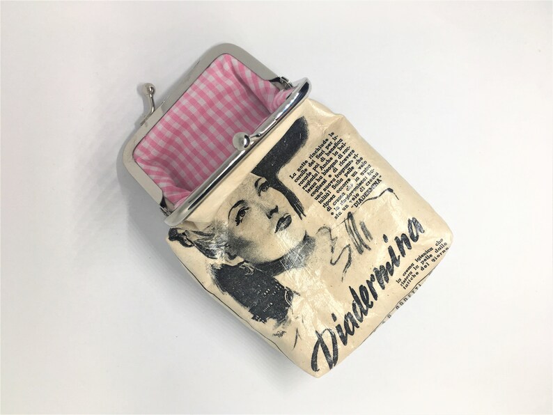 May include: A small, cream-colored coin purse with a silver clasp. The purse has a black and white image of a woman on the front, along with the text "Diadermina". The inside of the purse is lined with pink and white gingham.