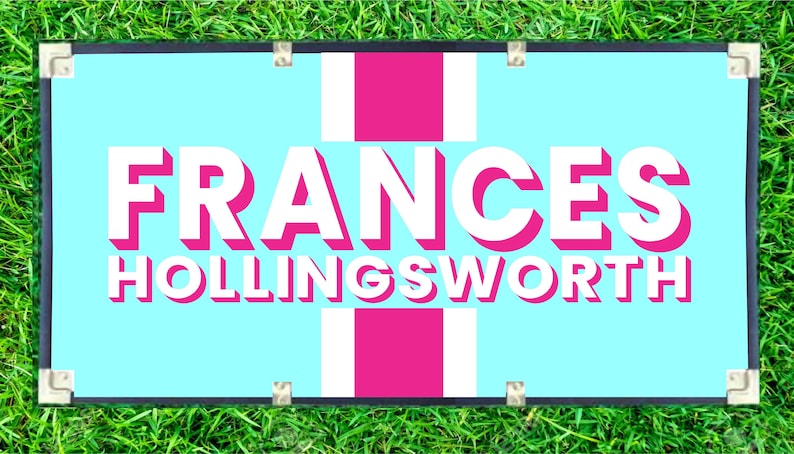 May include: A rectangular sign with the name "FRANCES HOLLINGSWORTH" in white, outlined in pink, on a light blue background. The sign has a pink cross design and is framed in black with silver corner protectors. The sign is placed on a bed of green grass.
