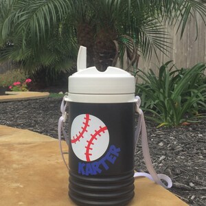May include: Black and white insulated water bottle with a white lid and a white strap. The bottle has a red and white baseball graphic and the name "Karter" in blue letters.