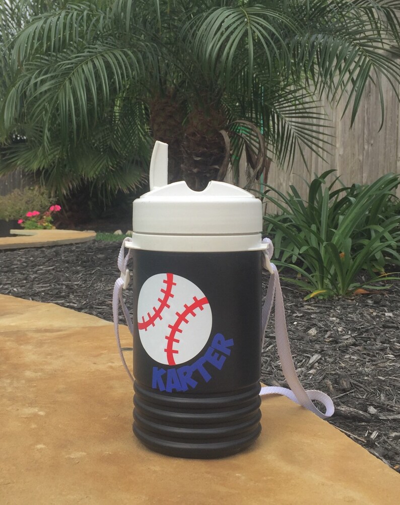 May include: Black and white insulated water bottle with a white lid and a white strap. The bottle has a red and white baseball graphic and the name "Karter" in blue letters.