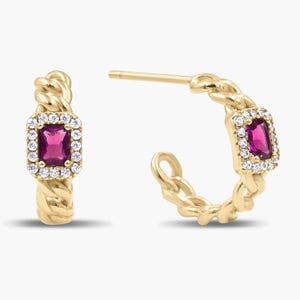 May include: A pair of gold hoop earrings featuring a twisted chain design. Each earring is centered with a rectangular, deep pink gemstone surrounded by a halo of small, clear white stones. The earrings include a post back closure mechanism.