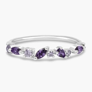 May include: A silver ring featuring an array of purple gemstones in various shapes. The ring's band is thin and polished, with the gemstones set across the top. The gemstones include oval, marquise, and round cuts, creating a sparkling, elegant design.