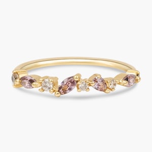 May include: A delicate gold ring featuring an array of small, marquise-cut and round gemstones in shades of pink and clear. The gemstones are set along the top of the ring band, creating a subtle, elegant design.