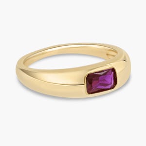 May include: A gold ring with a rectangular, deep purple gemstone. The ring has a smooth, rounded band and a bezel setting that holds the gemstone securely. The gemstone is a vibrant, eye-catching color.