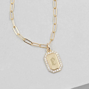 May include: Gold-toned necklace with a rectangular pendant. The pendant is outlined with small, clear stones and features the letter "P" in an elegant font. The chain has a paperclip link design.