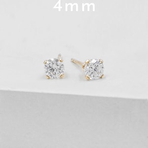 May include: A pair of gold stud earrings, each featuring a clear, round, 4 mm gemstone. The earrings are set in a simple, classic design, perfect for everyday wear. The background is a clean, white surface.