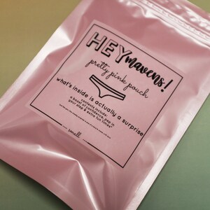 May include: A pink pouch with a white label that says "HEYmavens! pretty pink pouch what's inside is actually a surprise contents include: a boost of confidence, pep in your step & extra fun times" and "..... small"