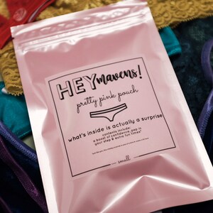 May include: A pink pouch with a white label that says "HEYmavens! pretty pink pouch what's inside is actually a surprise contents include: a boost of confidence, pep in your step & extra fun times" and "...small".