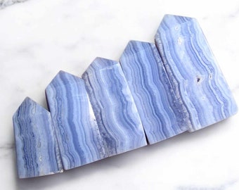 May include: A set of six blue agate crystal points, each with a unique pattern of blue and white banding. The points are arranged in a row, with the largest point at the top and the smallest point at the bottom.