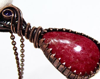 May include: A copper wire wrapped pendant featuring a red ruby gemstone with a smaller purple gemstone accent. The pendant is attached to a copper chain.