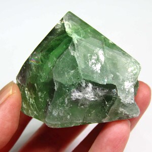 May include: A large, green fluorite crystal with a pyramid shape. The crystal has a translucent appearance and shows some internal striations.