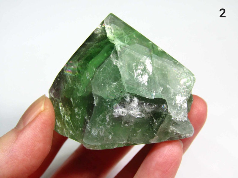 May include: A large, green fluorite crystal with a pyramid shape. The crystal has a translucent appearance and shows some internal striations.