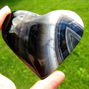 May include: A polished heart-shaped stone featuring a smooth, glossy surface with distinct bands of black, white, and gray. The stone displays a natural layered pattern with a prominent triangular design on the right side and the number 11.