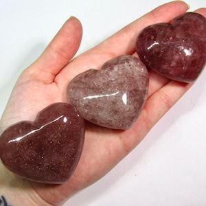 May include: Three heart-shaped polished rose quartz crystals in various shades of pink and brown.