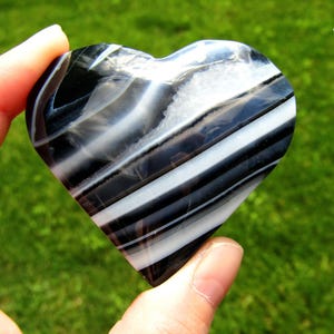 May include: A heart-shaped polished stone featuring alternating bands of black and white with a small crystalline inclusion near the top. The number 10 is printed in the upper right corner of the image against a natural green background.