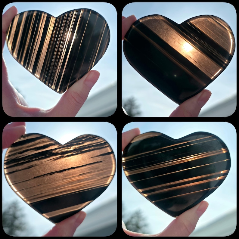 May include: Four heart-shaped stones with a striped pattern are displayed. The stones are held up against a bright sky. The stones have a dark brown and gold color scheme, with the stripes running across the heart shape.