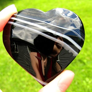 May include: A polished heart-shaped stone featuring a glossy black surface with distinct, horizontal white bands running across the upper portion. The stone has a smooth, reflective finish and is marked with the number 6 in the top right corner.