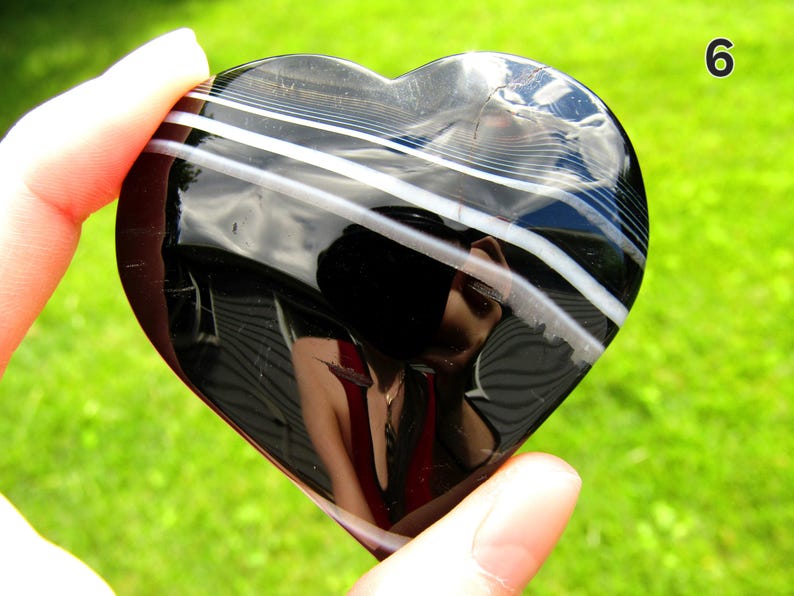 May include: A polished heart-shaped stone featuring a glossy black surface with distinct, horizontal white bands running across the upper portion. The stone has a smooth, reflective finish and is marked with the number 6 in the top right corner.
