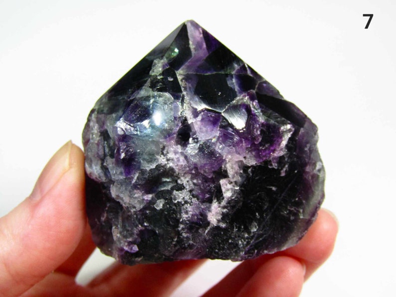 May include: A dark purple and green fluorite crystal point with a rough, natural surface. The crystal is about 2 inches tall and has a pointed tip.