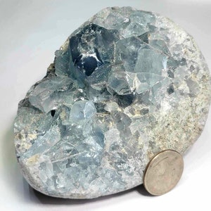 May include: A large, blue celestite geode with a rough exterior and a cluster of crystals inside. The geode is about the size of a US quarter.