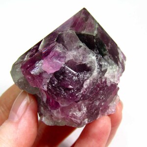 May include: A large, purple fluorite crystal with a pointed top and a rough, textured surface.