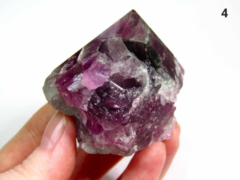 May include: A large, purple fluorite crystal with a pointed top and a rough, textured surface.