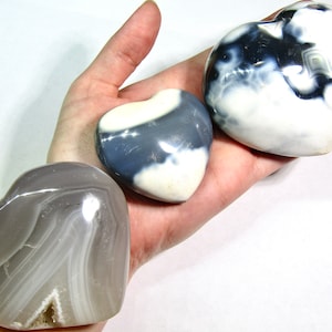 May include: Three heart-shaped agate stones in shades of gray and white. The stones are polished and have a smooth, glossy finish.